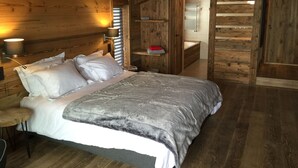 A wooden cabin bedroom with a bed, bedside lamp, and a view of a bathroom. - New chalet exceptional rated 5 *, conveniently located only Contamines (Les Contamines-Montjoie)