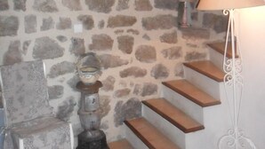 A room with a stone wall, a small table with a lamp, and a staircase with wooden steps. - L'Ostel Aveyronnais (golinhac)