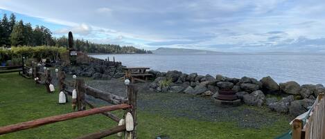 A waterfront park with picnic tables, a wooden fence, and a rocky shoreline.