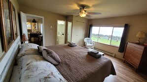 Un dormitorio con cama, ventilador de techo, ventana con vistas y una silla.