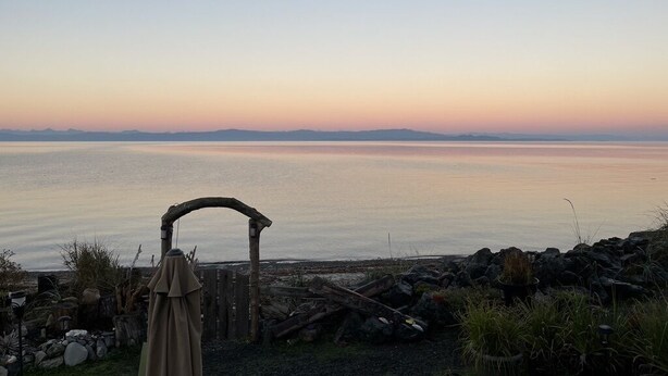 Vista costera con un arco de madera y una zona de estar cubierta con vista al mar.