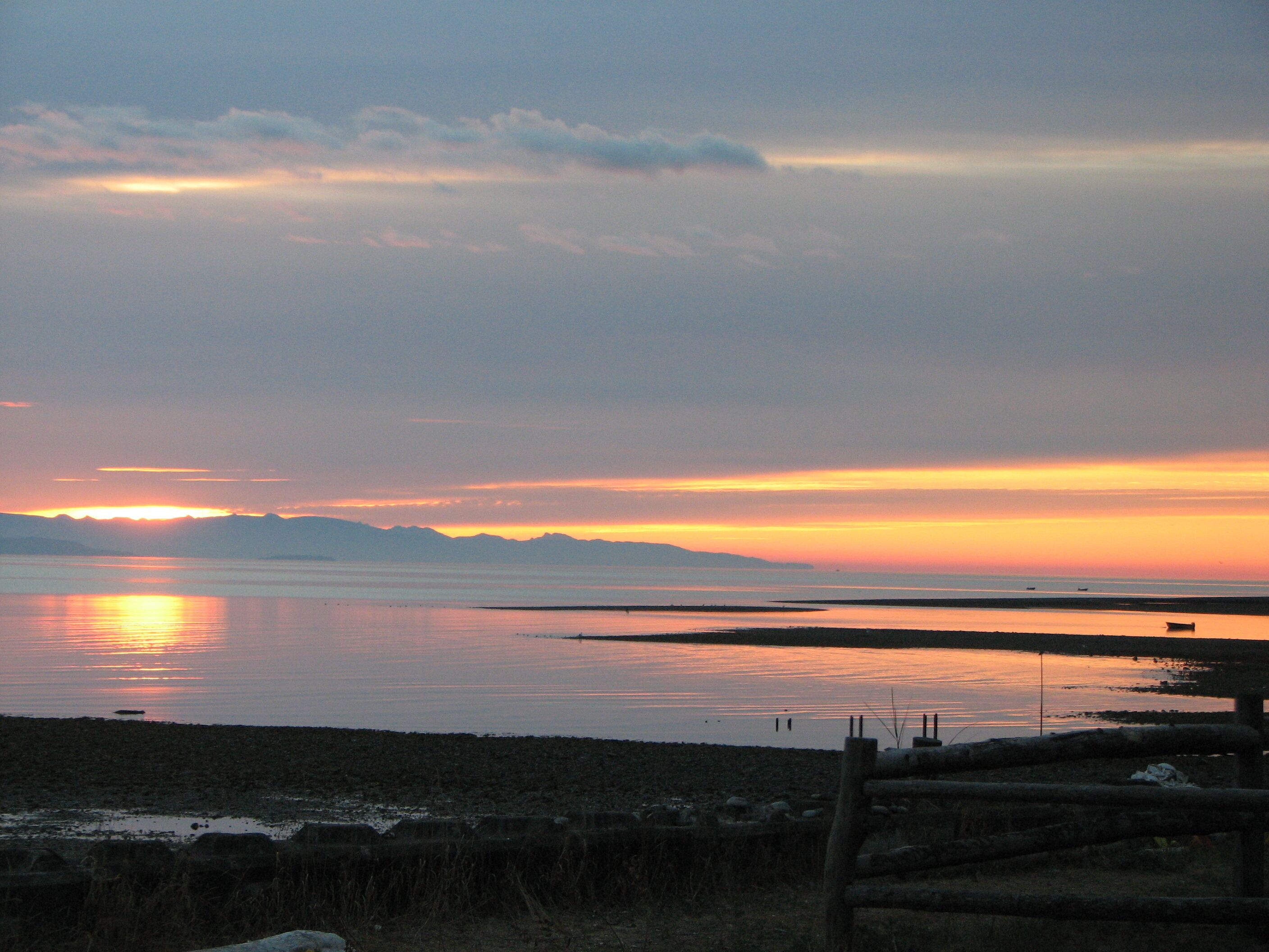 A sunset over a calm body of water with a distant mountain range.