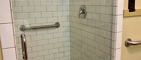 Eine Dusche mit weißen Fliesen, einer Glastür und einer Haltestange.