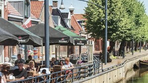 Un paseo fluvial con terrazas en cafés, un canal y edificios tradicionales con tejados rojos.