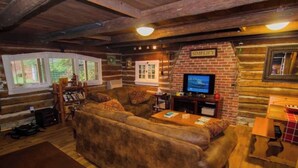 L’intérieur d’un chalet confortable, avec des murs en bois, un grand canapé marron, un téléviseur et une cheminée.