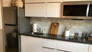 A modern kitchen with white cabinets, a stainless steel refrigerator, a microwave, and a wooden cutting board.