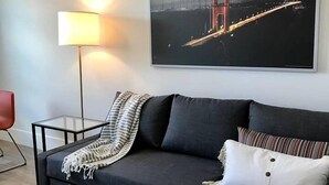 A modern living room with a dark grey sofa, a striped throw blanket, and a lamp. A large framed picture of the Golden Gate Bridge is on the wall.