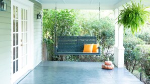 A porch with a dark green bench, white columns, and a hanging plant.