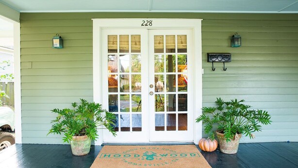 A front door with the number 228, two potted plants, a welcome mat, and two wall-mounted lanterns.