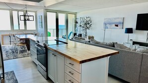 Eine moderne Küche mit Holztischplatte und weißen Schränken, ein Essbereich mit Stühlen, einem Sofa und einem Fernseher.