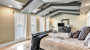 Een slaapkamer met een groot bed, een dressoir, een televisie en een raam met gordijnen.