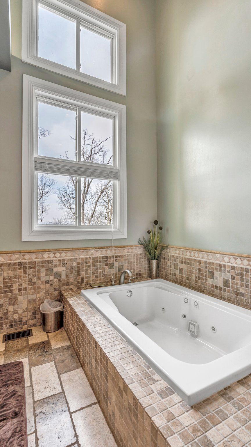 A bathroom with a large bathtub, a window with a view of bare trees, and a tiled backsplash.