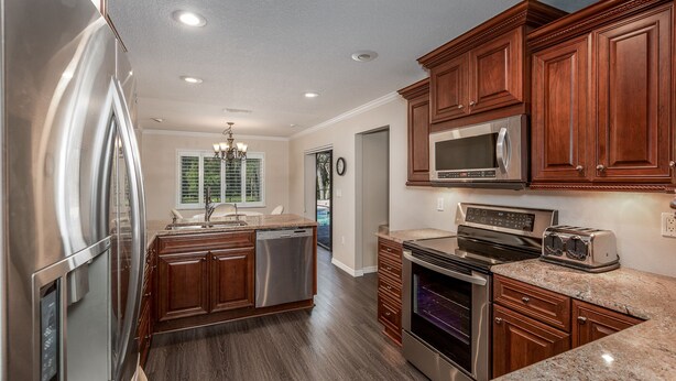 A modern kitchen with stainless steel appliances, wooden cabinets, and granite countertops. - Cozy home, rural setting, near Gulf Beaches (New Port Richey)
