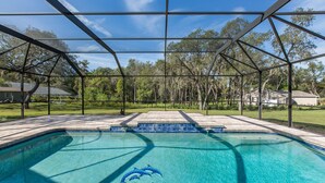 A clear blue swimming pool with dolphin decals, surrounded by a covered patio with a view of trees and houses. - Cozy home, rural setting, near Gulf Beaches (New Port Richey)