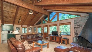 Un amplio salón con sofás de cuero, una mesa de centro, una chimenea y grandes ventanales con vistas al exterior.