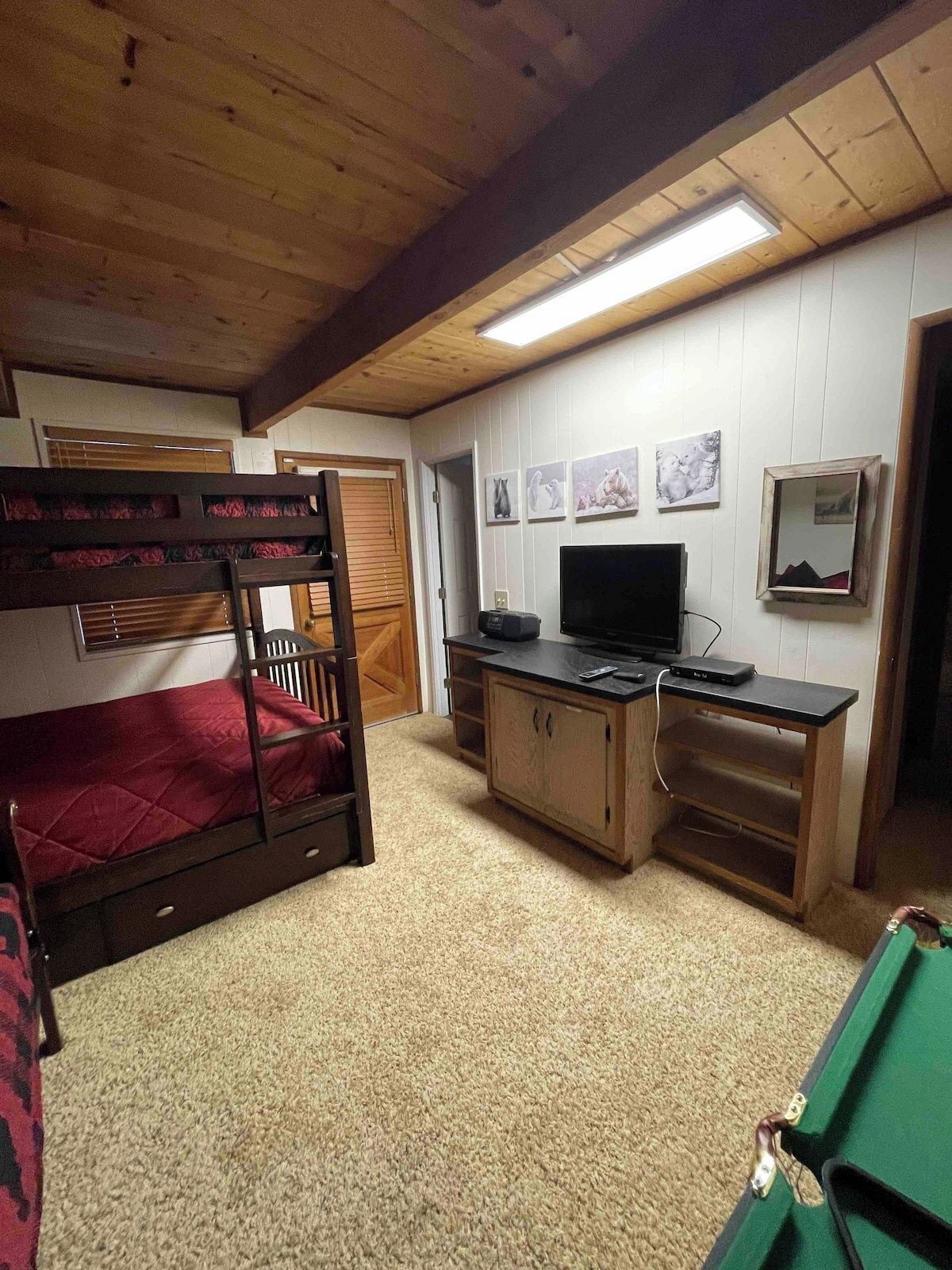A bunk bed with a red mattress, a wooden desk with a flat-screen TV, and a carpeted floor.