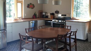 Una cocina con techo de madera, luces colgantes, una mesa de comedor con sillas y vistas a árboles a través de amplios ventanales.