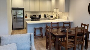 A modern kitchen with white cabinets, a stainless steel refrigerator, and a dining area with wooden chairs and a table.
