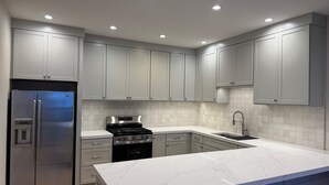 A modern kitchen with grey cabinets, stainless steel appliances, and a marble countertop.