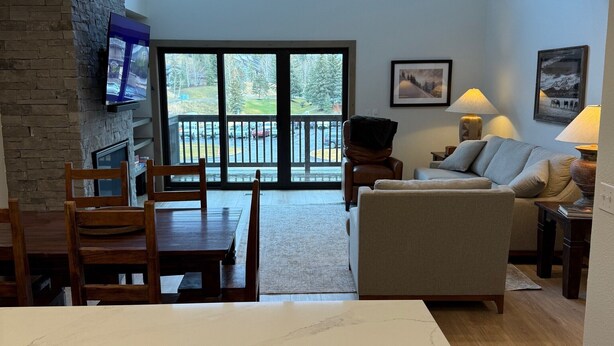 A spacious living area with a dining table, chairs, a sofa, and a TV mounted on a stone wall.