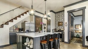Una cucina moderna con un'isola centrale, sgabelli da bar, illuminazione a sospensione e una scala che conduce a un altro piano.