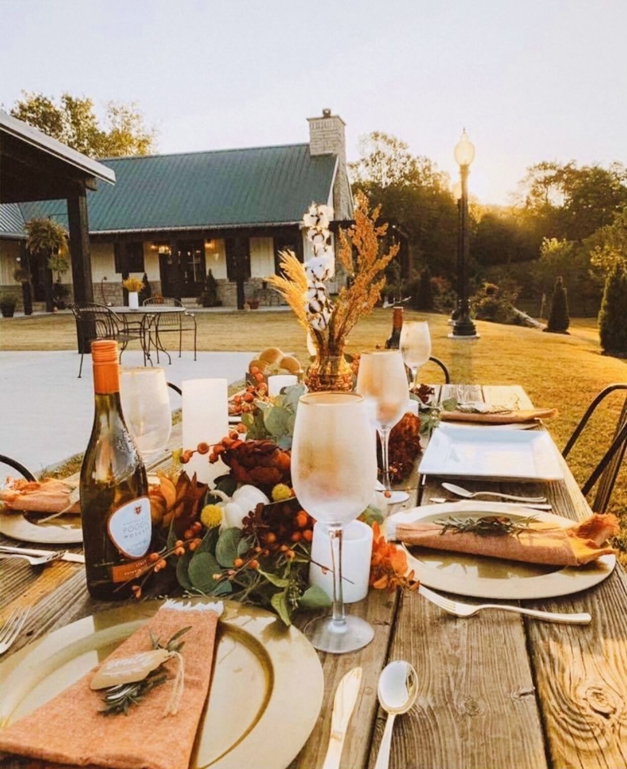 An outdoor dining table set with plates, cutlery, wine glasses, and a bottle.