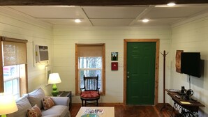 A cozy living room with a wooden table, a green door, and a television mounted on the wall.