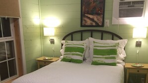 A bedroom with a bed, green walls, two bedside lamps, an air conditioner, and a window with blinds.