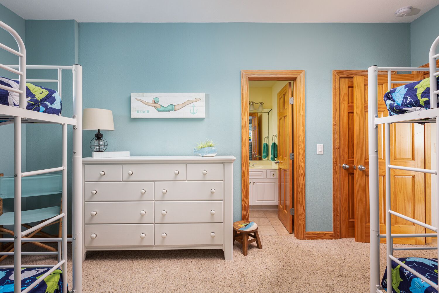 A bedroom with bunk beds, a dresser, a small stool, and a painting on the wall.
