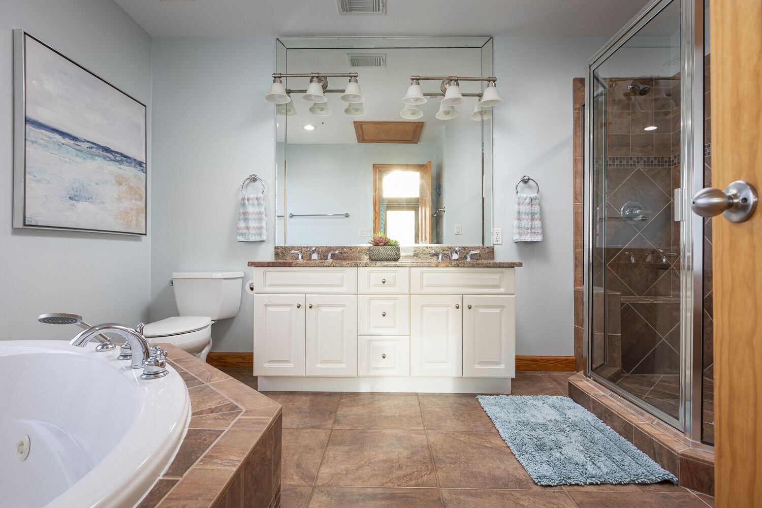 A modern bathroom with a large bathtub, a walk-in shower, and a vanity with a mirror and lights.