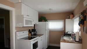 Una cocina compacta con electrodomésticos blancos, una encimera y una ventana con persianas.