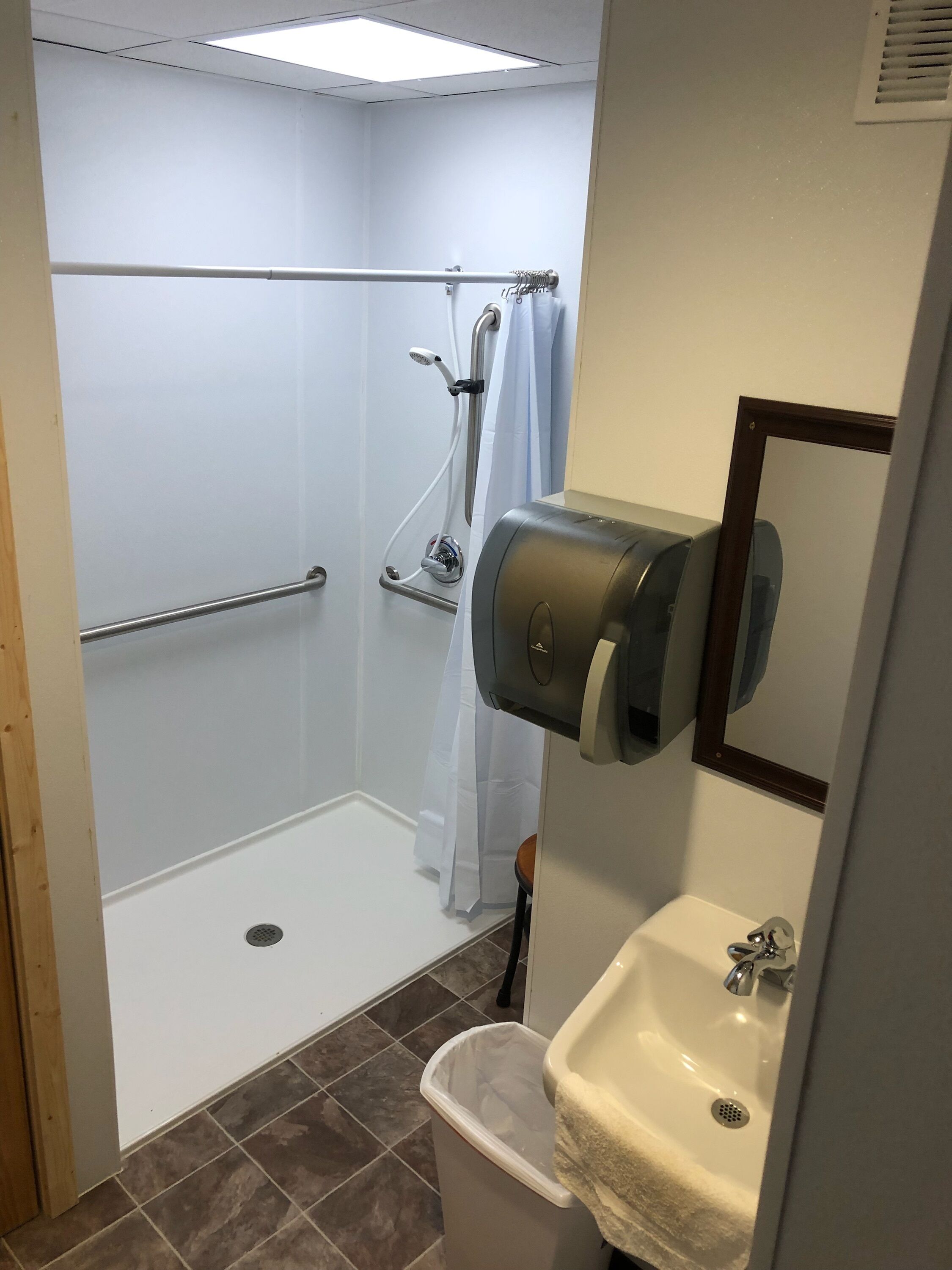 A bathroom with a shower, a hand dryer, a sink, and a trash can.