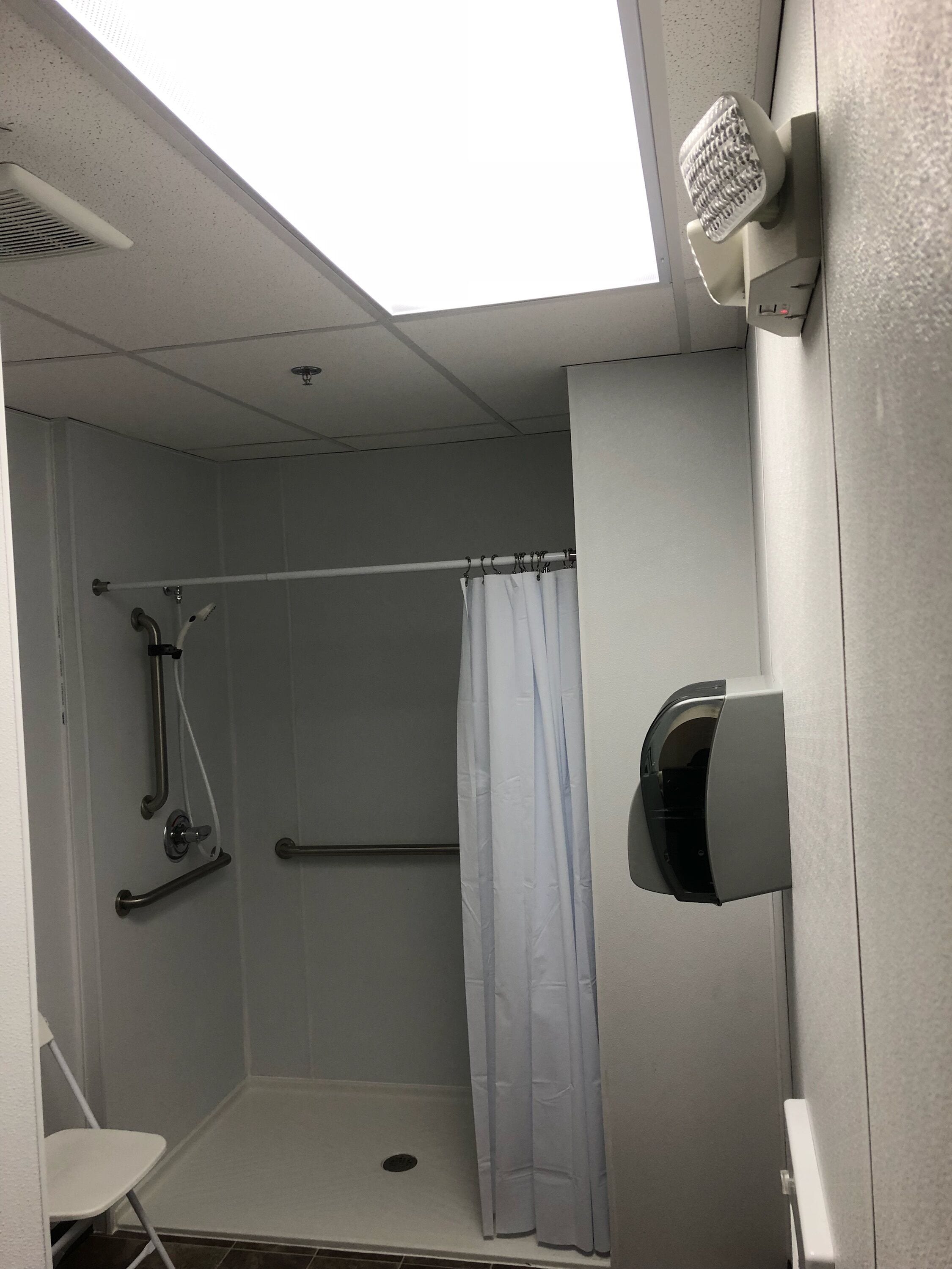 A small, enclosed shower area with a white shower curtain, a handheld showerhead, and a wall-mounted soap dispenser.