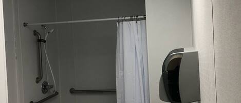A small, enclosed shower area with a white shower curtain, a handheld showerhead, and a wall-mounted soap dispenser.