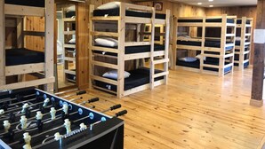 A room with bunk beds, wooden floors, and a foosball table.