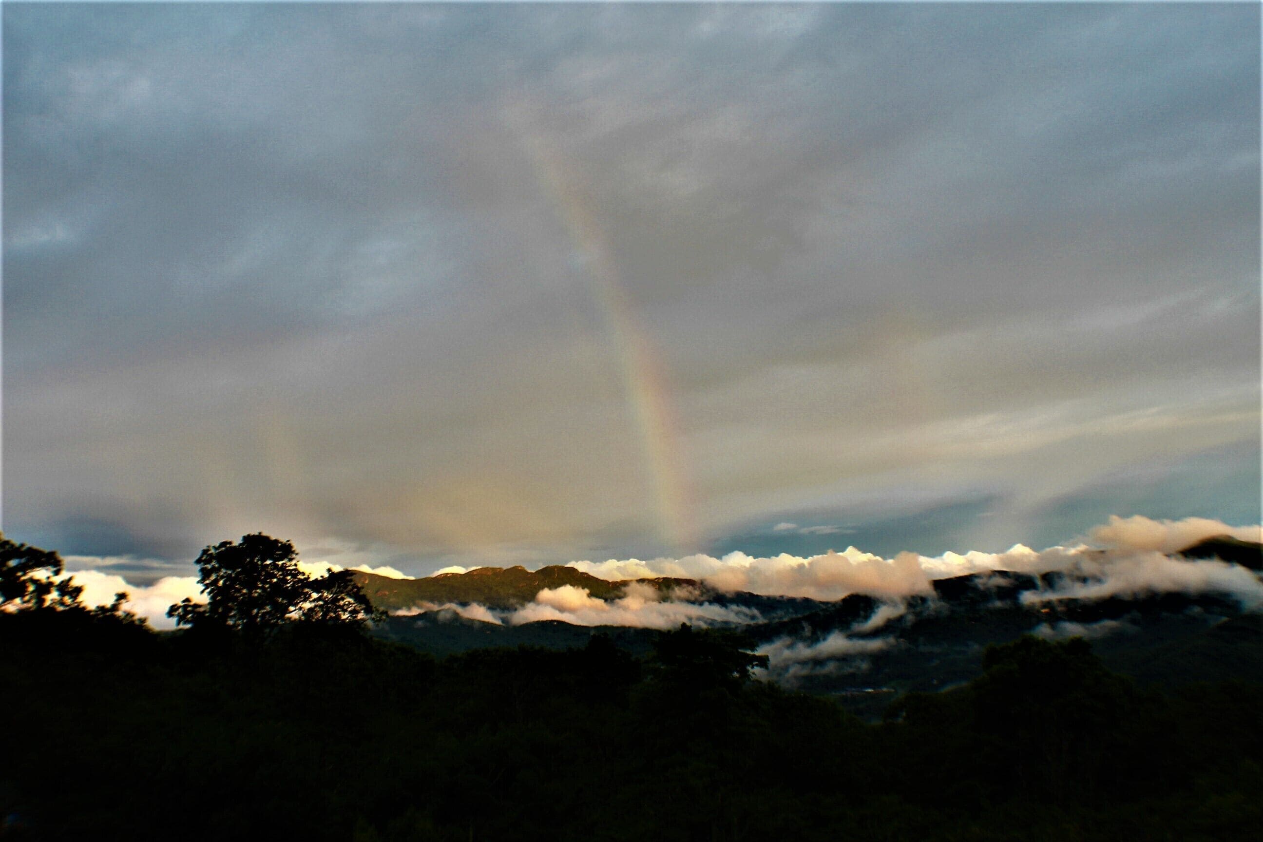 A mountain landscape with a rainbow and clouds.