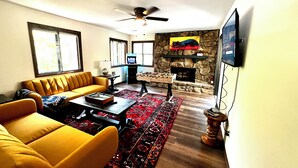 Ein Wohnzimmer mit gelber Couch, Couchtisch, Kamin, Steinwand und Wandfernseher.