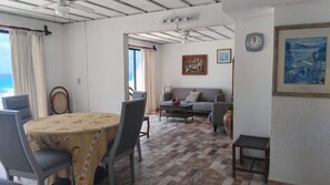 A dining area with a table and chairs, a sofa, and a coffee table. There is a window with curtains, a clock on the wall, and a framed painting. - Sleep by the Blue Paradise (Cancun)