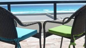 Zwei Korbstühle mit blauen und grünen Kissen auf einem Balkon mit Blick auf einen Strand.