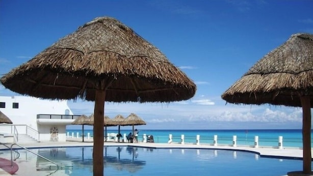 Ein Poolbereich mit Strohdächern, blauem Himmel und Blick aufs Meer.
