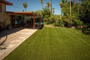 Un patio trasero con un porche, piscina y césped bien cuidado.