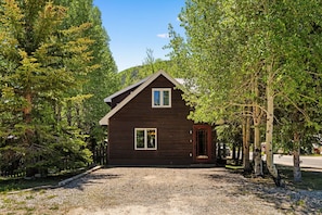 A wooden cabin with a gravel driveway, surrounded by trees.