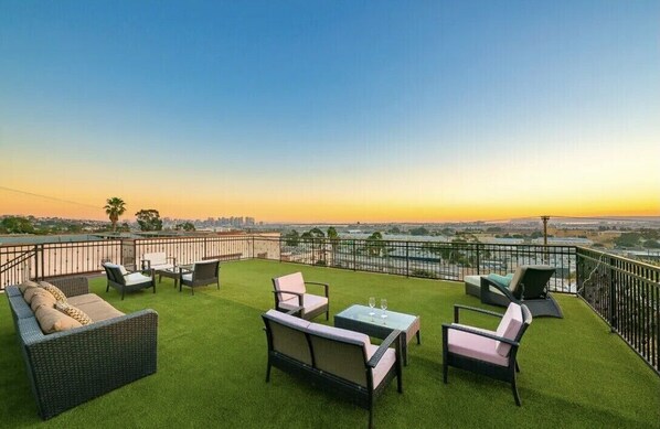 A rooftop terrace with outdoor furniture, a view of the city skyline, and a sunset.