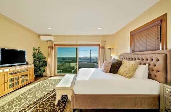 Habitación de hotel con una cama grande, televisión, planta y vistas a la ciudad a través del ventanal.