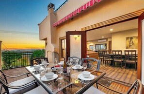 A dining area with a table set for two, a balcony with a view, and a room with a bed and a painting.