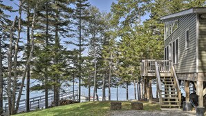 A wooden cabin with a deck and a staircase leading to a second level, overlooking a lake with a dock and boats. - Enjoy the quiet, the calm, the sunset and the deck! (Cushing)