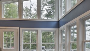 A cozy room with a large window, a wooden bench, and a blue storage unit. - Enjoy the quiet, the calm, the sunset and the deck! (Cushing)