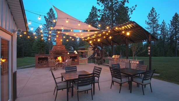 Eine Terrasse im Freien mit Kamin aus Ziegelsteinen, einem Holztisch und -stühlen sowie Lichterketten.