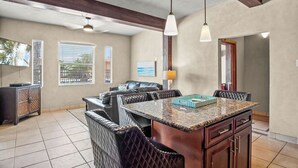 A spacious living area with a large island, leather seating, and a view of palm trees through the windows. - Shadow Palm Villa 3 Private Resort Villa (Port Aransas)
