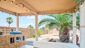 A covered outdoor patio with a barbecue grill, seating area, and palm trees. - Shadow Palm Villa 3 Private Resort Villa (Port Aransas)